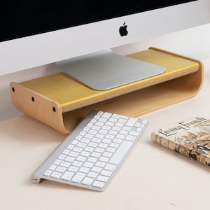 May include: A wooden monitor stand with a yellow top and a shelf underneath. A white keyboard and a white mouse are on the desk in front of the stand. A book titled "Living French" is also on the desk.