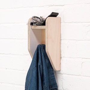May include: A wooden wall-mounted shelf with a small shelf and a hook. A blue denim shirt is hanging on the hook. The shelf has a few items on it, including a phone and keys.