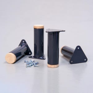 May include: Four black metal furniture legs with a wood top. The legs are triangular shaped and have a screw hole on each side. The legs are arranged in a semi-circle on a gray surface.