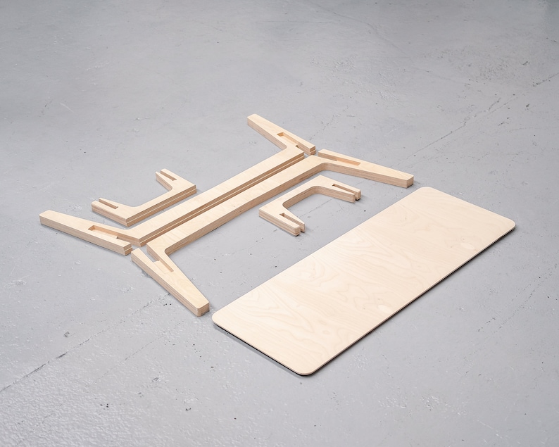 Puede incluir: Una mesa de madera de paquete plano con un acabado de madera clara. La mesa est&aacute; desmontada y colocada sobre una superficie gris. La superficie de la mesa es rectangular y las patas est&aacute;n hechas de cuatro piezas de madera que encajan entre s&iacute;.