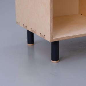 May include: A wooden shelf unit with black legs. The shelf unit is made of plywood and has a simple design.