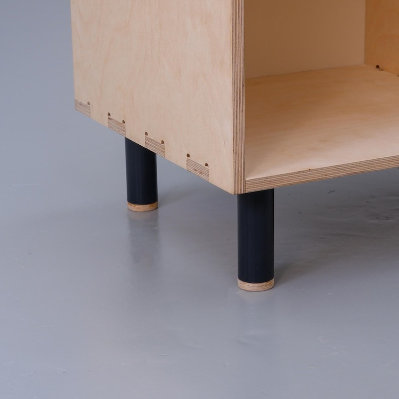 May include: A wooden shelf unit with black legs. The shelf unit is made of plywood and has a simple design.
