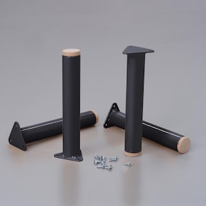 Könnte beinhalten: Vier schwarze Möbelbeine aus Metall mit Holzaufsätzen. Die Beine sind an der Basis dreieckig und haben eine zylindrische Form. Die Beine sind in einem Halbkreis angeordnet, mit Schrauben, die vor ihnen verstreut sind.