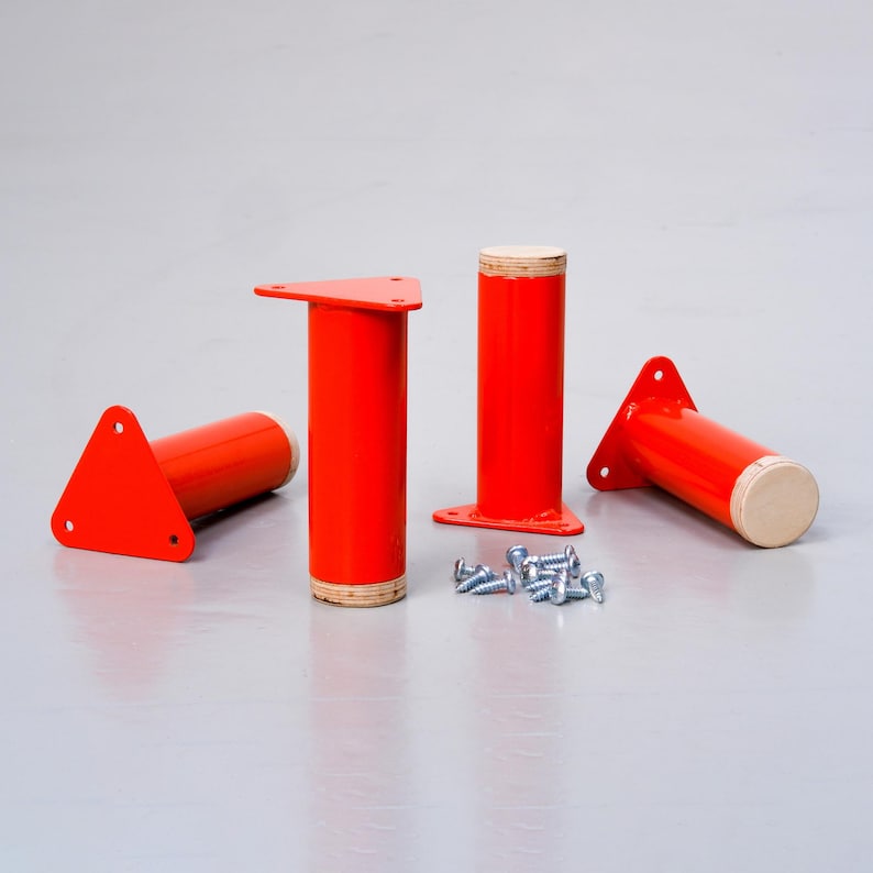 May include: Four red metal furniture legs with triangular bases and wood tops. The legs are arranged on a gray surface with a scattering of silver screws.