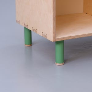 May include: A wooden shelf unit with four green painted legs. The shelf unit is made of plywood and has a simple, modern design.