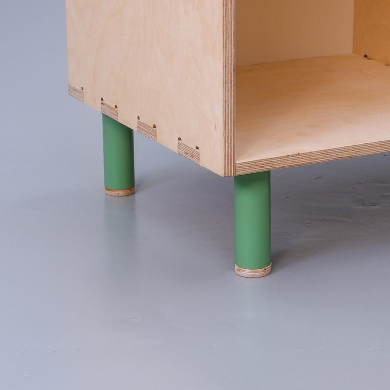 May include: A wooden shelf unit with four green painted legs. The shelf unit is made of plywood and has a simple, modern design.