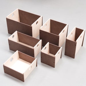 May include: A set of six wooden storage boxes in different sizes. The boxes have a two-tone design, with brown exteriors and natural wood interiors. Each box has a circular handle cutout on the sides.