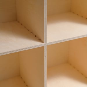 May include: A close-up of a wooden shelf unit with four empty square compartments. The shelves are made of light-colored wood and have a smooth, unfinished surface.