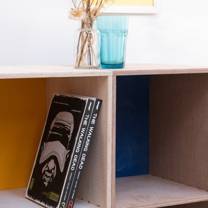 May include: A wooden shelf unit with three shelves, painted in yellow, blue, and natural wood. Two graphic novels titled "The Walking Dead" are on the shelf.