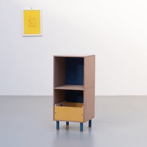 May include: A small, two-shelf wooden cabinet with a drawer. The cabinet is brown with blue accents and a yellow drawer. The cabinet is standing on four blue legs.