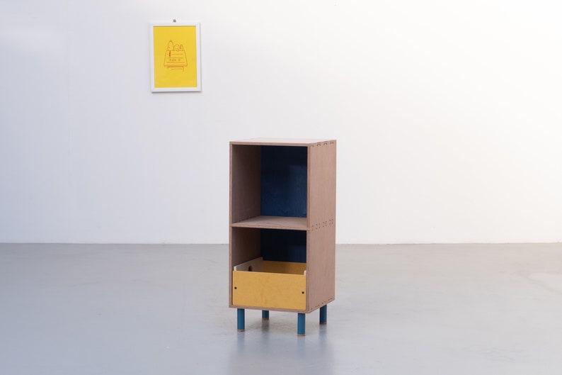May include: A small, two-shelf wooden cabinet with a drawer. The cabinet is brown with blue accents and a yellow drawer. The cabinet is standing on four blue legs.