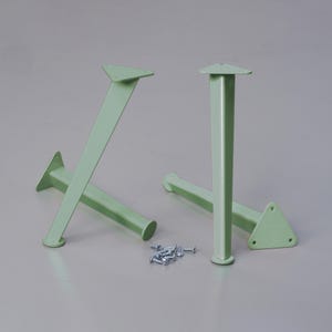 Può includere: Due set di gambe per tavolo in metallo di colore verde chiaro. Ogni gamba ha una base triangolare e una parte superiore quadrata. Le gambe sono in metallo e hanno una finitura liscia.