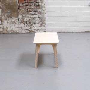 Puede incluir: Una mesa de centro de madera clara con una tapa rectangular y cuatro patas. La mesa est&aacute; sobre un suelo de hormig&oacute;n gris.