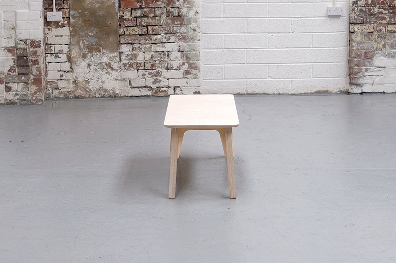 Puede incluir: Una mesa de centro de madera clara con una tapa rectangular y cuatro patas. La mesa est&aacute; sobre un suelo de hormig&oacute;n gris.