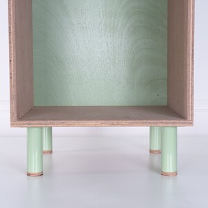 May include: A light green wooden shelf unit with four legs. The shelf is empty and has a light wood finish.