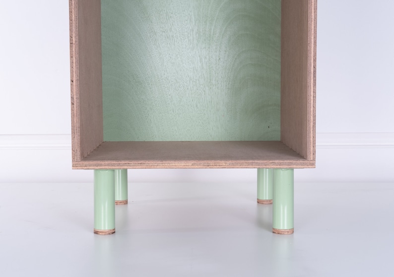 May include: A light green wooden shelf unit with four legs. The shelf is empty and has a light wood finish.