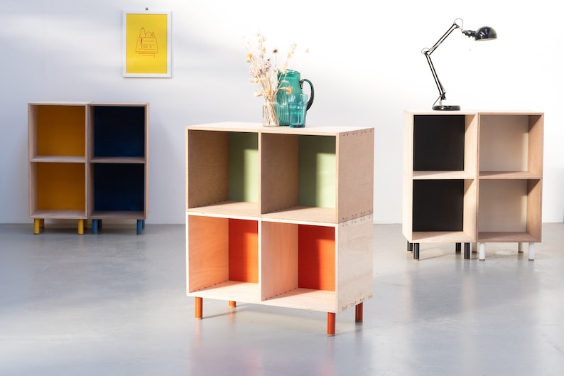 May include: Four wooden cube shelves with different colored interiors. The shelves are stacked on top of each other and have wooden legs. The shelves are painted yellow, blue, green, and orange.