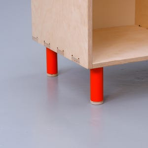 May include: A simple, wooden shelf unit with four red legs. The shelf is made of plywood and has a natural wood finish.