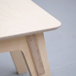 Puede incluir: Primer plano de una mesa de madera clara con un dise&ntilde;o simple y moderno. La mesa tiene un borde liso y redondeado y una sola pata visible en la imagen.
