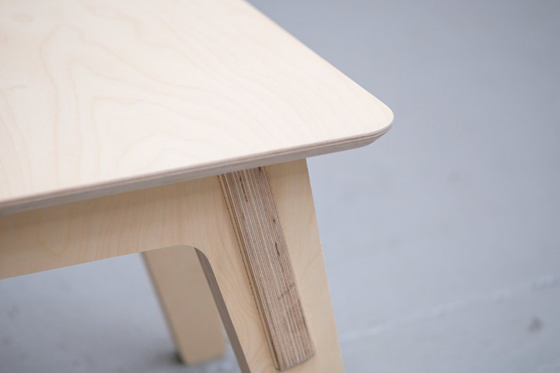 Puede incluir: Primer plano de una mesa de madera clara con un dise&ntilde;o simple y moderno. La mesa tiene un borde liso y redondeado y una sola pata visible en la imagen.