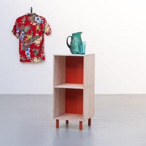 May include: A two-shelf wooden bookcase with orange painted shelves and legs. A green pitcher and glass are on the top shelf.