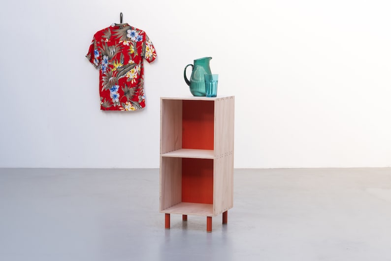 May include: A two-shelf wooden bookcase with orange painted shelves and legs. A green pitcher and glass are on the top shelf.