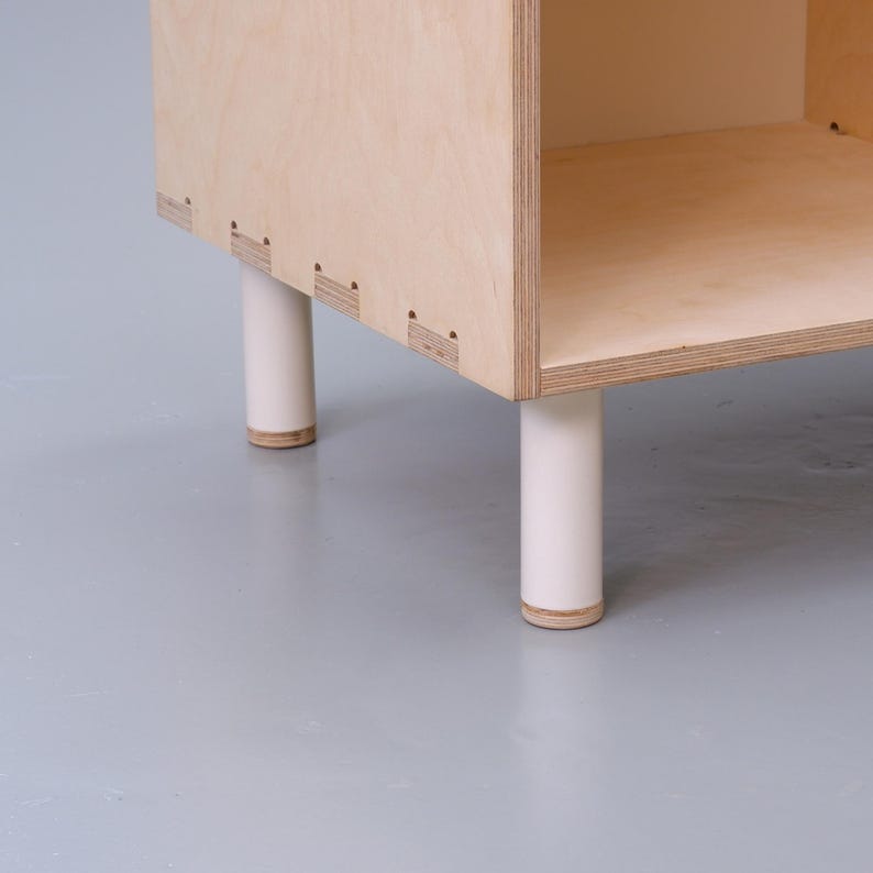May include: A wooden shelf unit with four white legs. The shelf is made of plywood and has a simple, modern design.