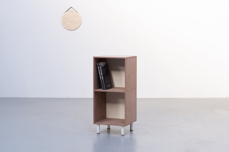 May include: A two-shelf wooden bookcase with white legs. The bookcase is brown and has a light brown interior. There are three books on the top shelf.