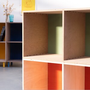 May include: A wooden bookshelf with six open compartments. The compartments are painted in different colors, including yellow, blue, green, and orange.
