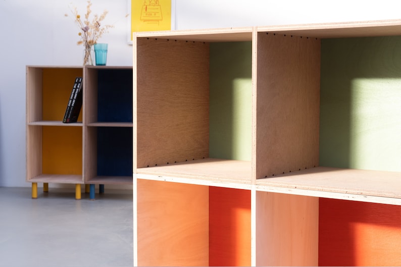 May include: A wooden bookshelf with six open compartments. The compartments are painted in different colors, including yellow, blue, green, and orange.