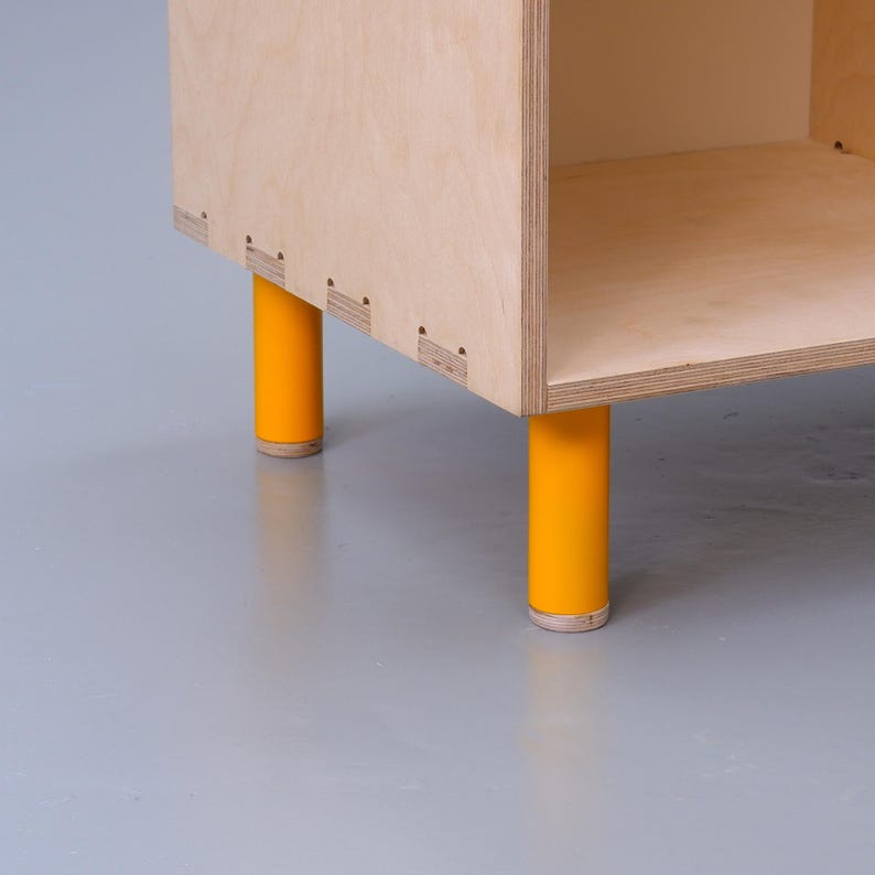 May include: A wooden shelf unit with four yellow legs. The shelf unit is made of plywood and has a simple, modern design.