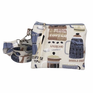 May include: A small, rectangular cream-colored zippered pouch with a blue and brown coffee-themed pattern. The pattern includes coffee pots, coffee beans, and the words "FRESH AMERICANO" and "DOUBLE SHOT." A matching lanyard with a silver clasp is attached.