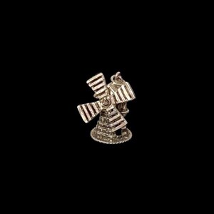 May include: A silver-colored windmill charm with detailed blades and a textured base. The charm is set against a black background, highlighting its intricate design and craftsmanship. A miniature representation of a classic Dutch windmill.