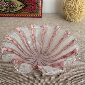 May include: A clear glass bowl featuring a scalloped edge and a decorative pattern of alternating white latticino mesh stripes and solid pink glass ribbons that radiate from the centre towards the ruffled rim of the vessel.