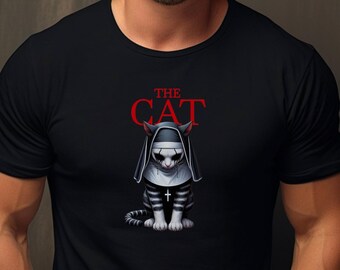 May include: Black t-shirt featuring a graphic of a cat dressed as a nun, with the text "THE CAT" in red above the cat. The cat graphic is in shades of gray and white, with a cross on its chest.