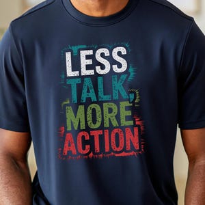 Puede incluir: Una camiseta azul marino con un gráfico colorido que dice "Less Talk More Action".
