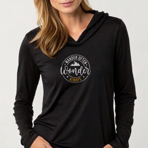 Puede incluir: Camiseta negra de manga larga con capucha y un gráfico blanco que dice "Wander Often, Wonder Always" en un círculo con un diseño de montaña.