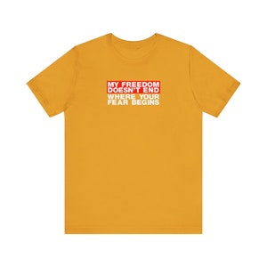 Op de afbeelding: Een geel T-shirt met een rode doos met de tekst "My Freedom Doesn't End Where Your Fear Begins" in witte letters.