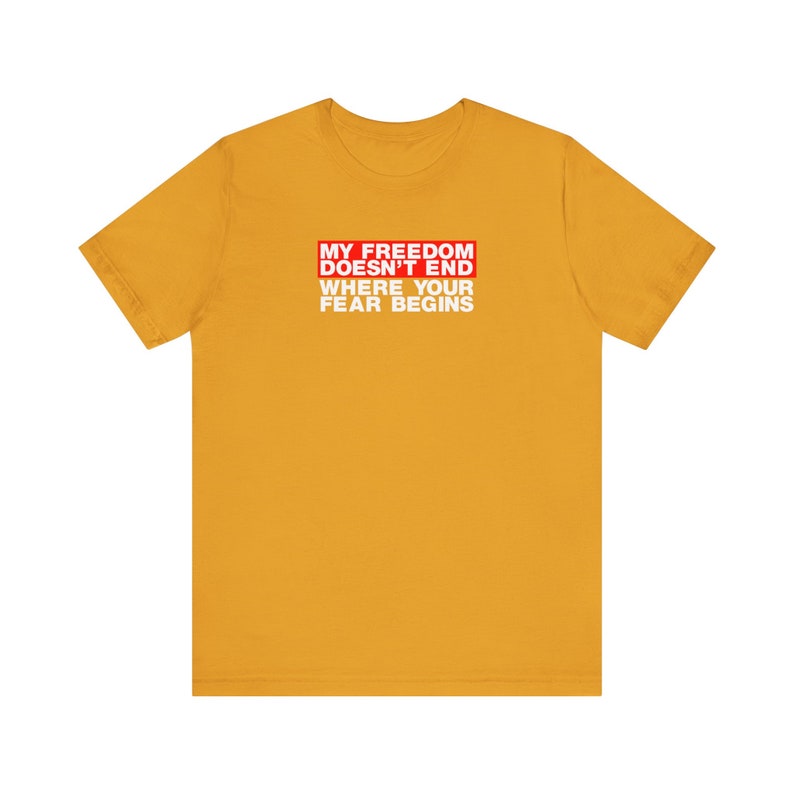 Op de afbeelding: Een geel T-shirt met een rode doos met de tekst "My Freedom Doesn't End Where Your Fear Begins" in witte letters.