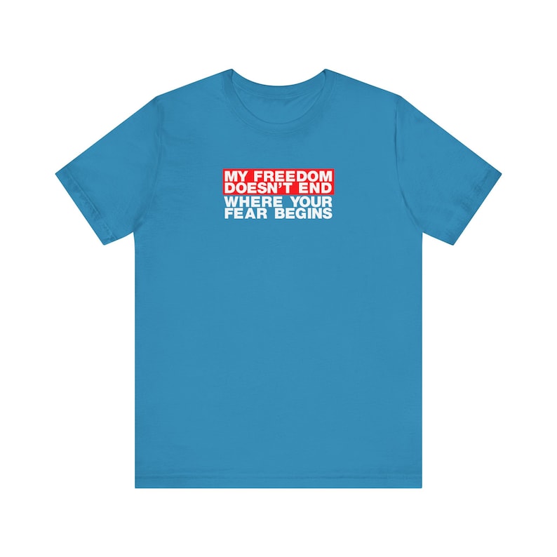 Op de afbeelding: Een lichtblauw t-shirt met een rode rechthoek waarop staat "My Freedom Doesn't End Where Your Fear Begins".