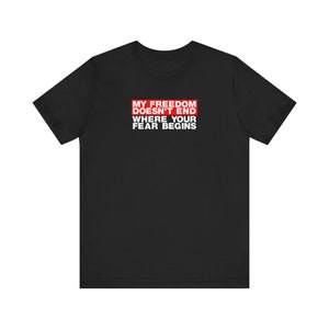 Op de afbeelding: Zwart T-shirt met een rode rechthoek en witte tekst die "Mijn vrijheid eindigt niet waar jouw angst begint." luidt.