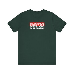 Op de afbeelding: Een donkergroen T-shirt met een rode doos met de tekst "My Freedom Doesn't End Where Your Fear Begins" in witte letters.