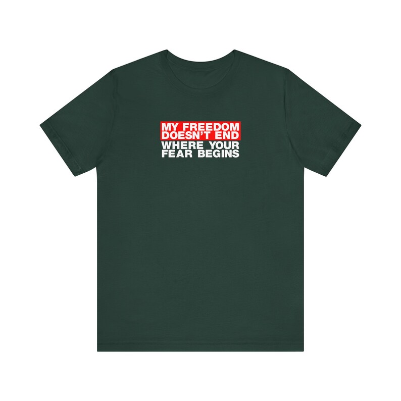 Op de afbeelding: Een donkergroen T-shirt met een rode doos met de tekst "My Freedom Doesn't End Where Your Fear Begins" in witte letters.