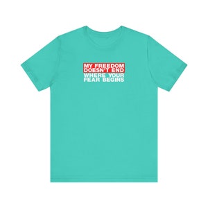 Op de afbeelding: Turquoise t-shirt met een rode rechthoek en witte tekst die "My Freedom Doesn't End Where Your Fear Begins" luidt.