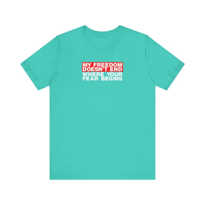 Op de afbeelding: Turquoise t-shirt met een rode rechthoek en witte tekst die "My Freedom Doesn't End Where Your Fear Begins" luidt.