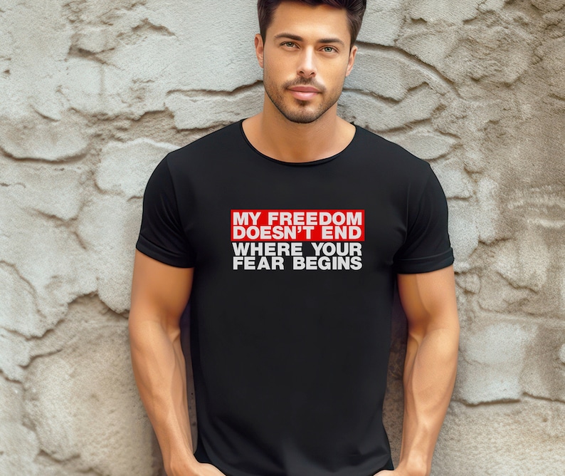 Op de afbeelding: Een zwart T-shirt met een rode rechthoek en witte tekst die "Mijn vrijheid eindigt niet waar jouw angst begint." luidt.