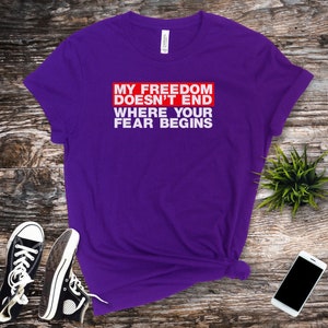 Op de afbeelding: Paars T-shirt met witte tekst die "My Freedom Doesn't End Where Your Fear Begins" zegt in een rode box.