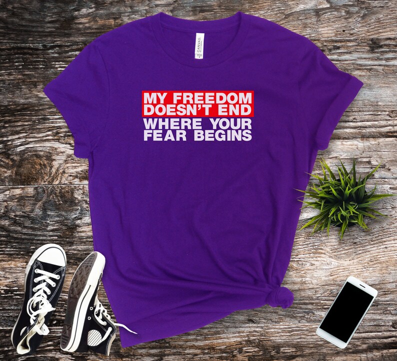 Op de afbeelding: Paars T-shirt met witte tekst die "My Freedom Doesn't End Where Your Fear Begins" zegt in een rode box.
