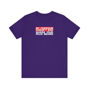 Op de afbeelding: Paars T-shirt met een rode doos met de tekst "Mijn vrijheid eindigt niet waar jouw angst begint".