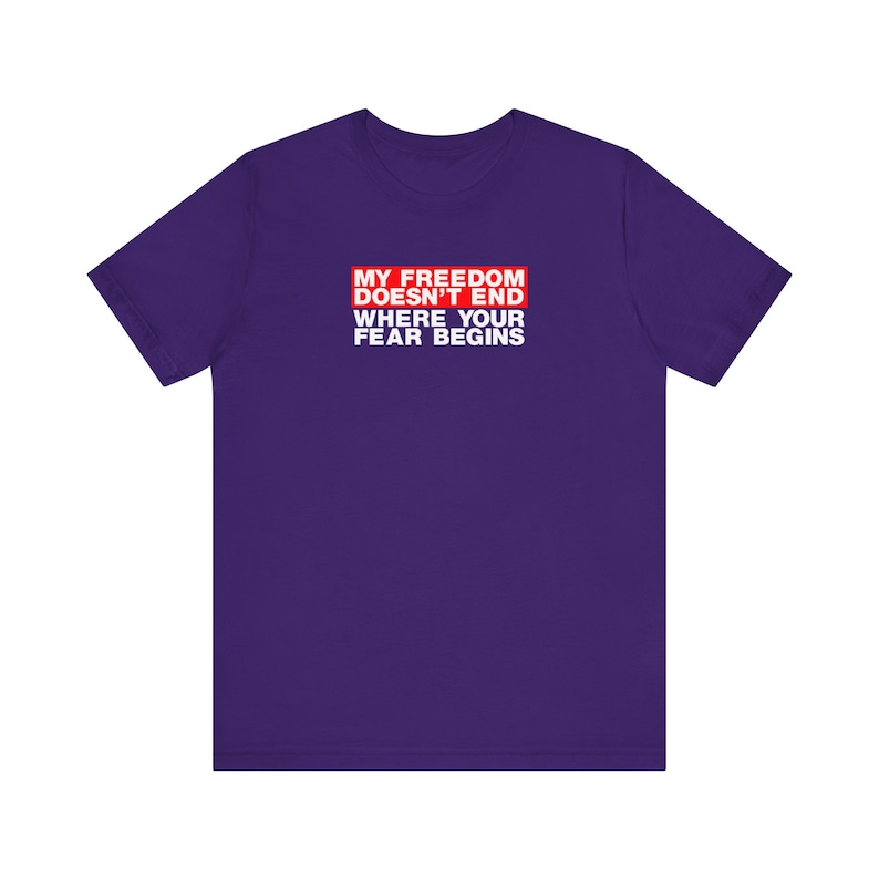Op de afbeelding: Paars T-shirt met een rode doos met de tekst "Mijn vrijheid eindigt niet waar jouw angst begint".